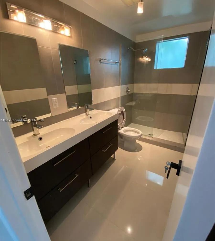 Modern bathroom with double sink vanity, glass shower, and toilet.